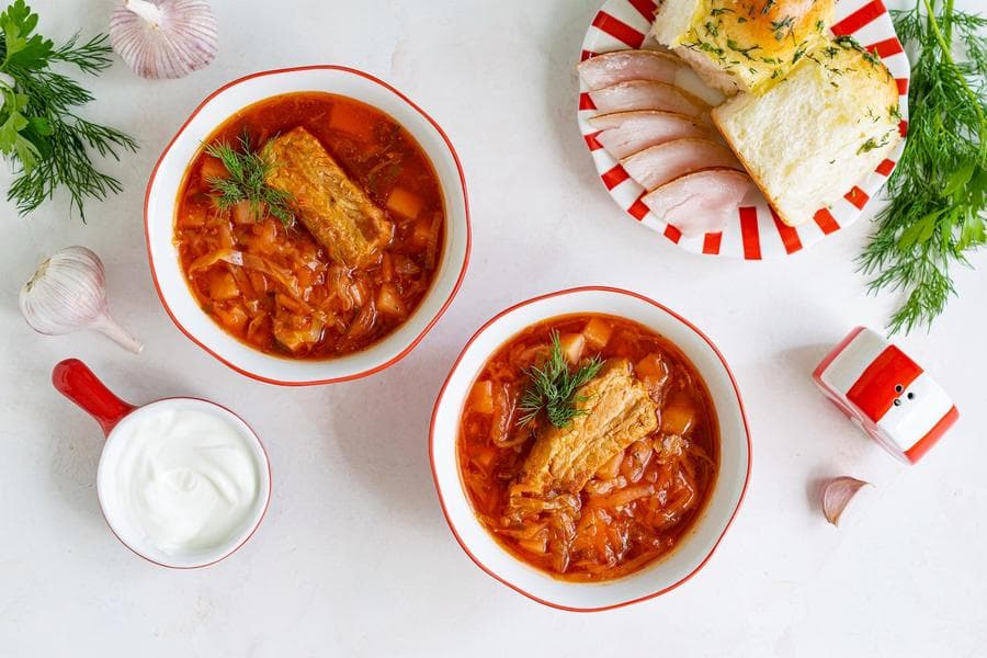Two bowls of borscht with bread, sour cream and fresh dill